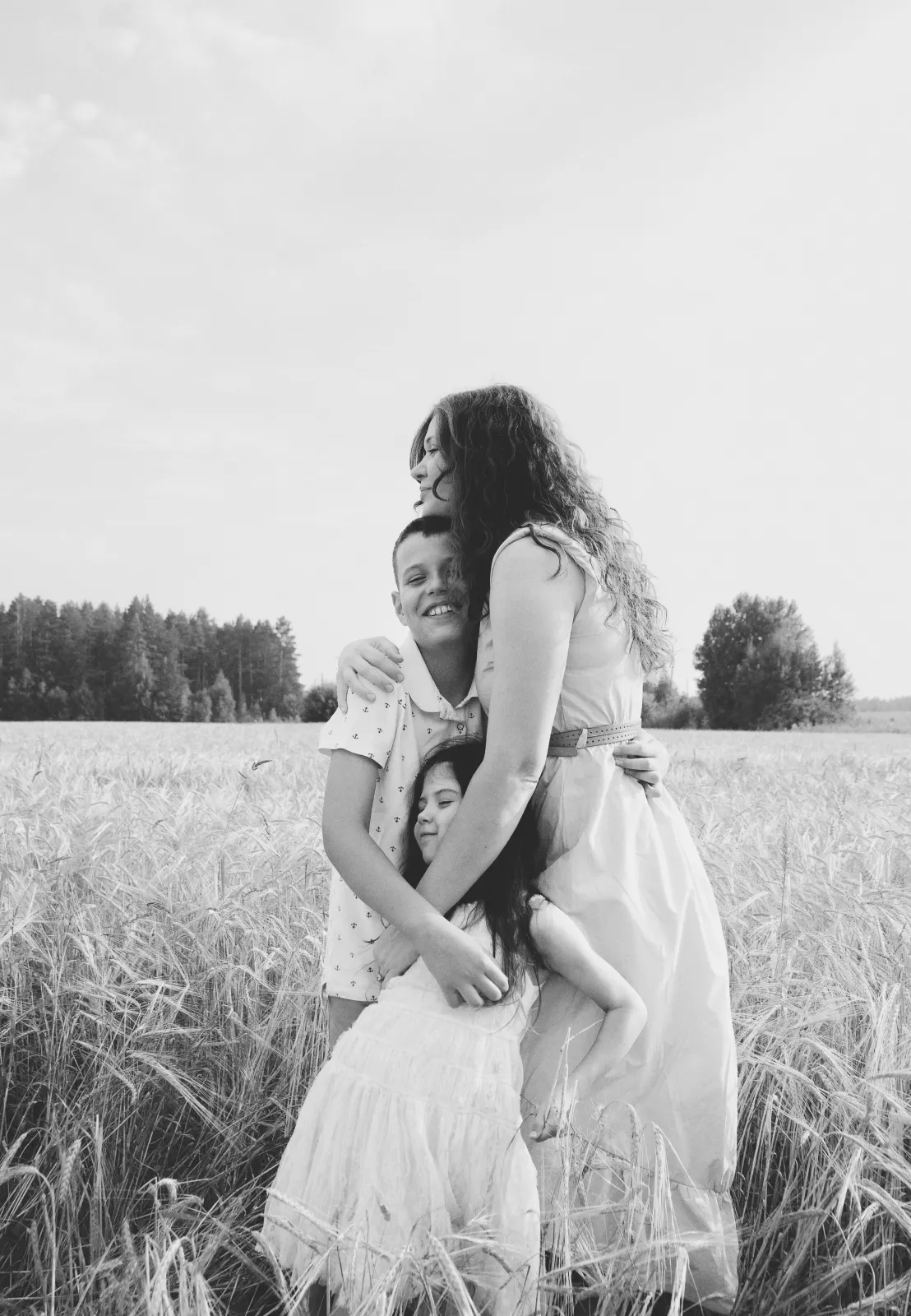 Black and white photo of a mother embracing her two children in a field