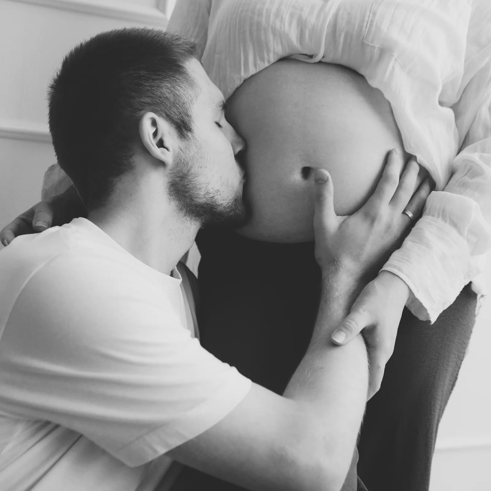 Black and white photo of a man kissing his partner's pregnant belly