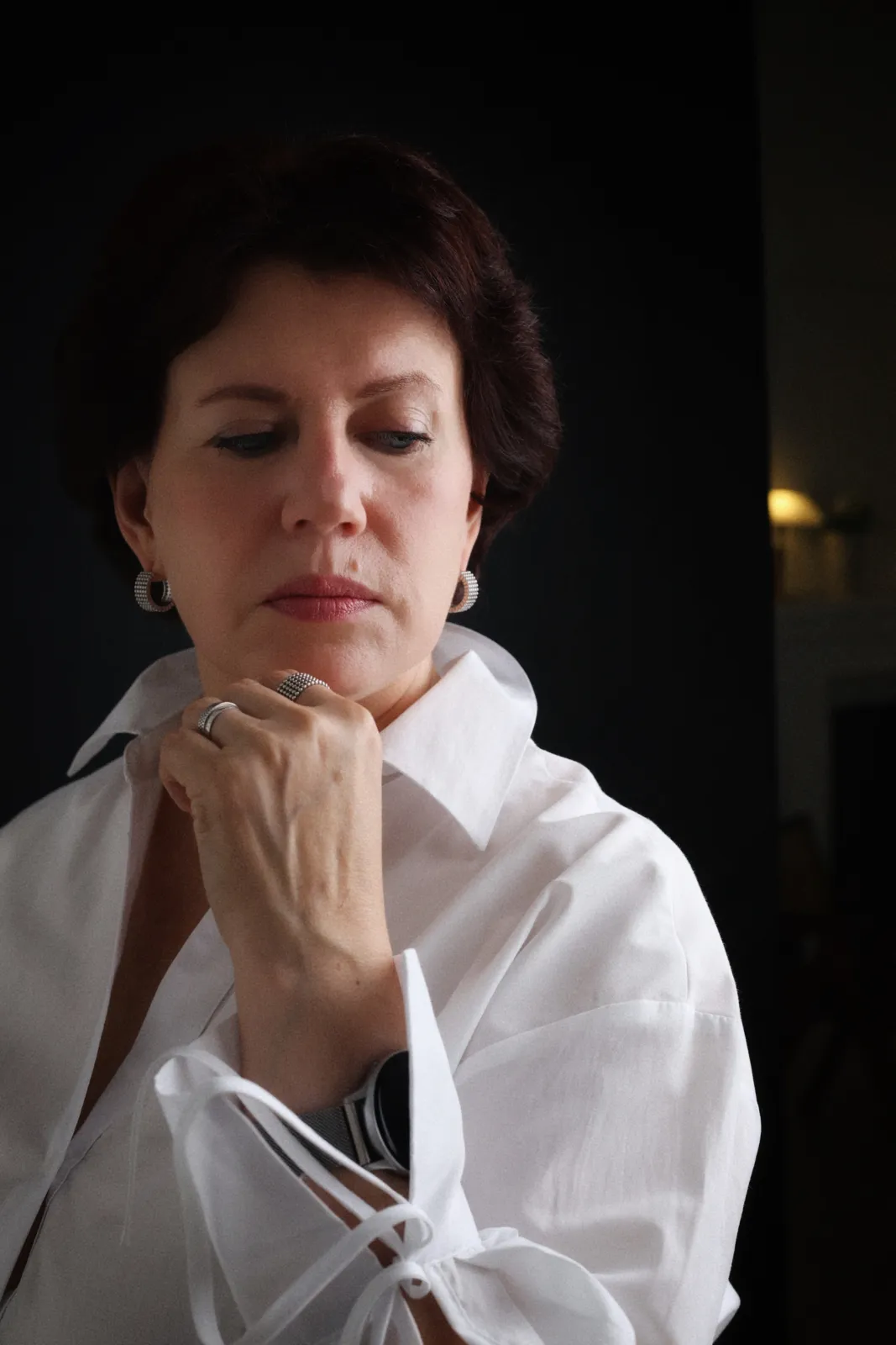 Low-key portrait of a woman in a white shirt against a dark background, lost in thought