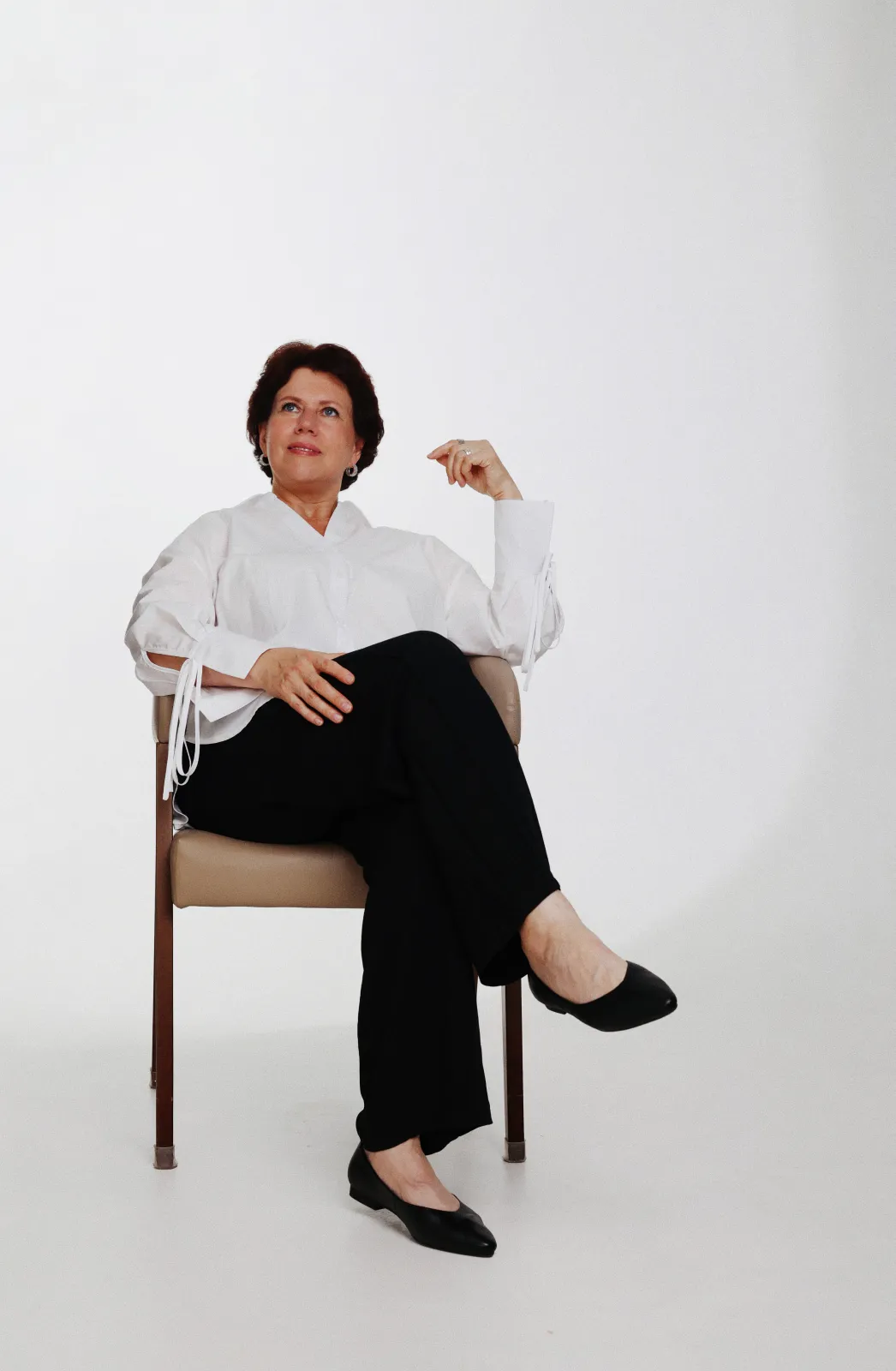 Studio portrait of a woman in a white shirt seated on a chair against a white backdrop